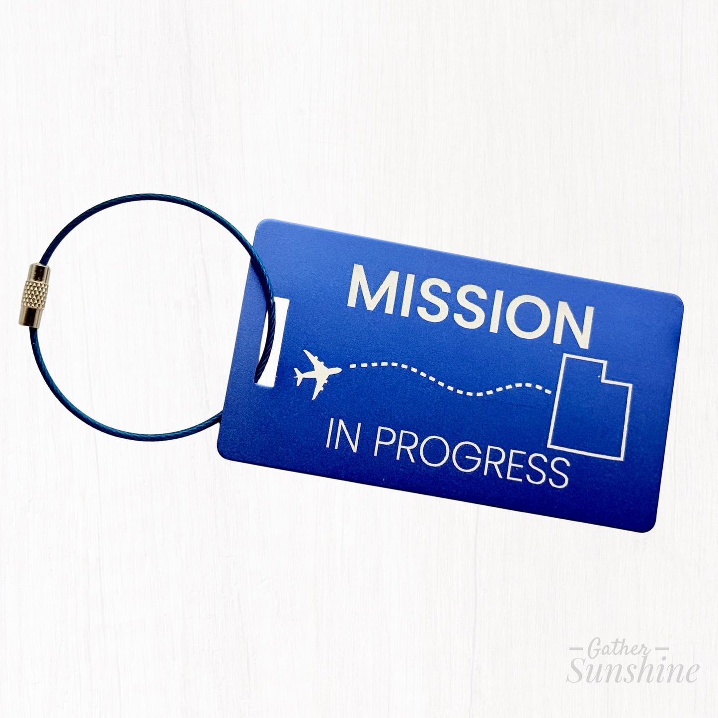 Blue “Mission in Progress” large luggage tag with airplane path flying to outlined Utah. Engraved LDS missionary tag by GatherSunshine.