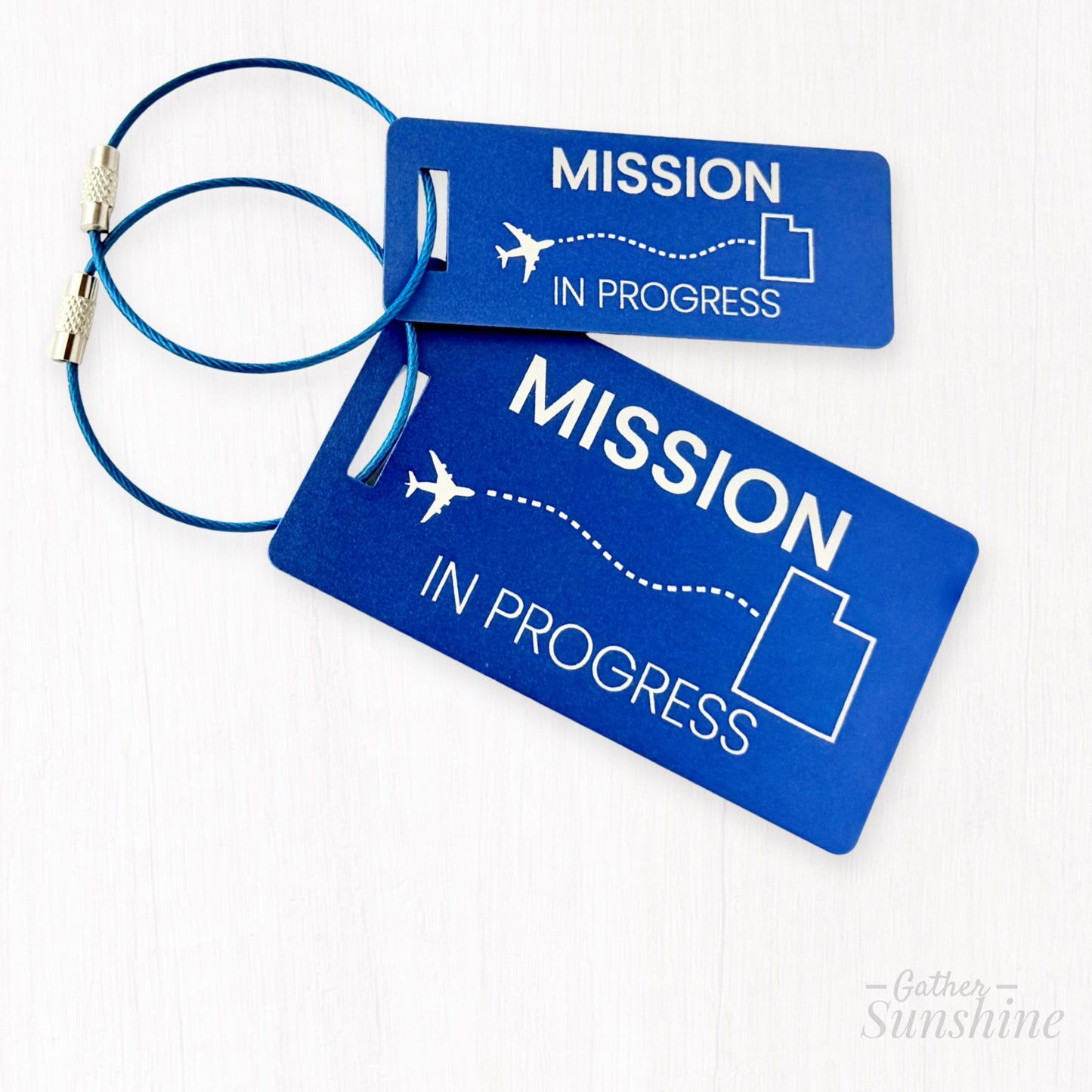 Blue “Mission in Progress” luggage tags in small and large sizes with airplane path flying to outlined Utah state. Personalized LDS missionary gift by GatherSunshine.