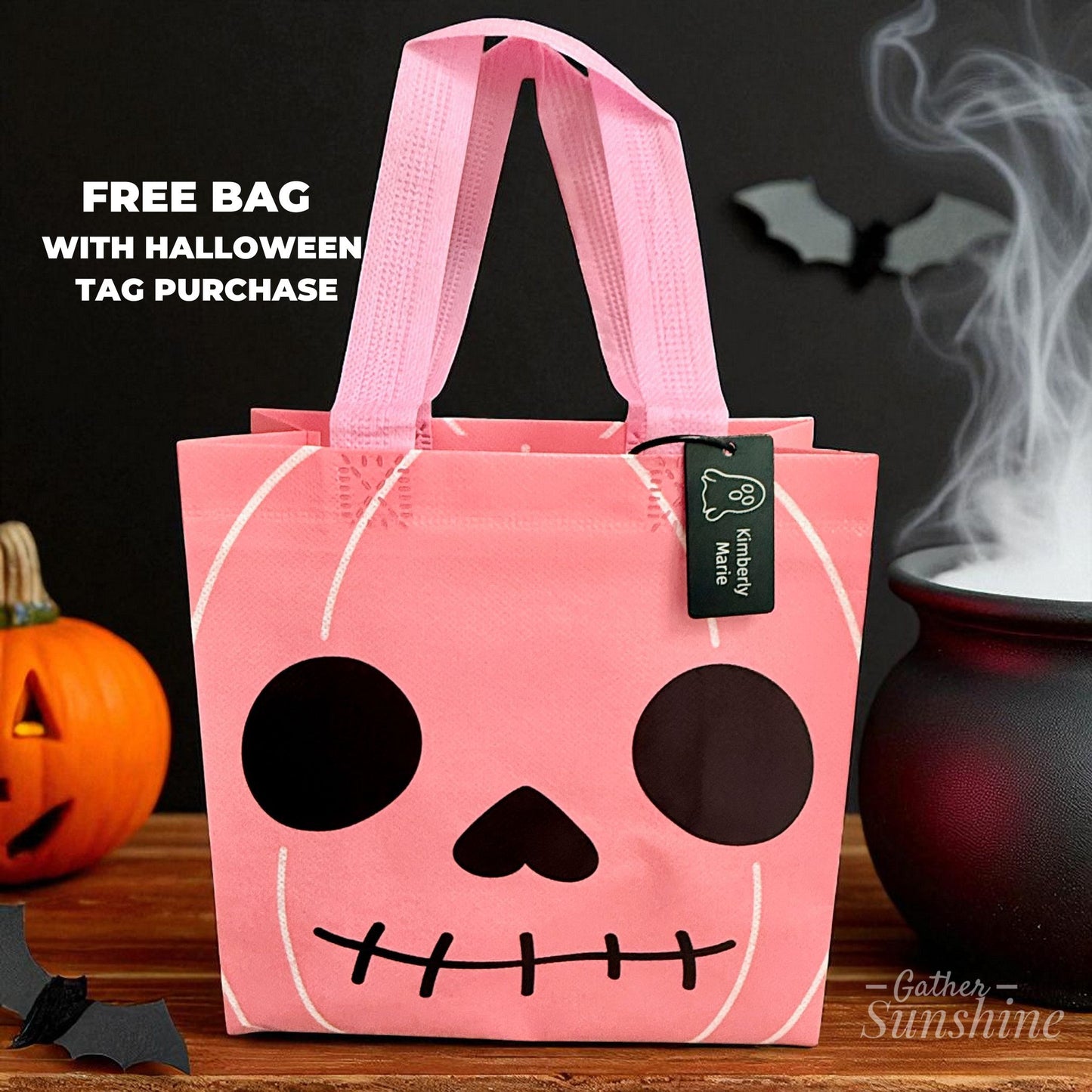 Pink pumpkin-shaped bag with black face design with a ghost black engraved tag set against a Halloween Background. #GatherSunshine