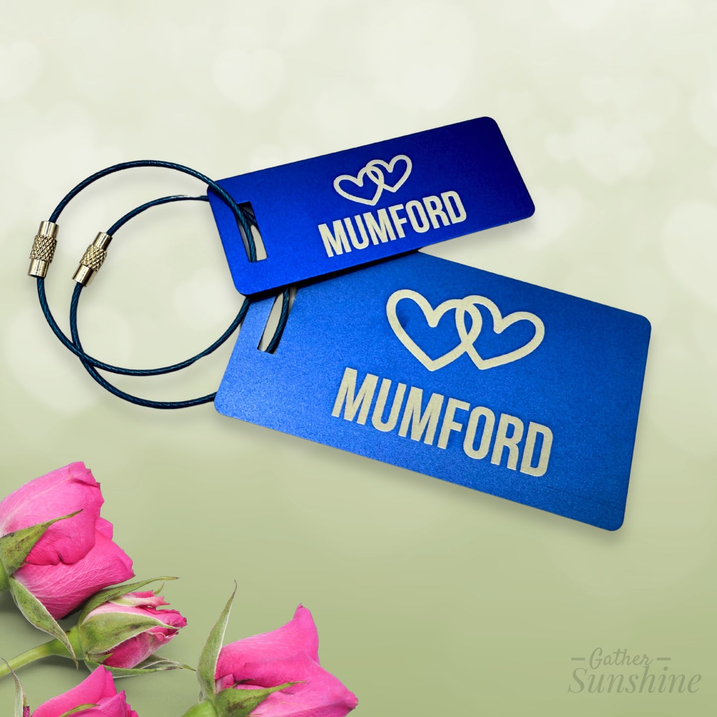 Small (3"x1") and large (3.5"x2") blue luggage tags customized with name of choice and two interlocking hearts on a light green background. Personalized engraving by Gather Sunshine.