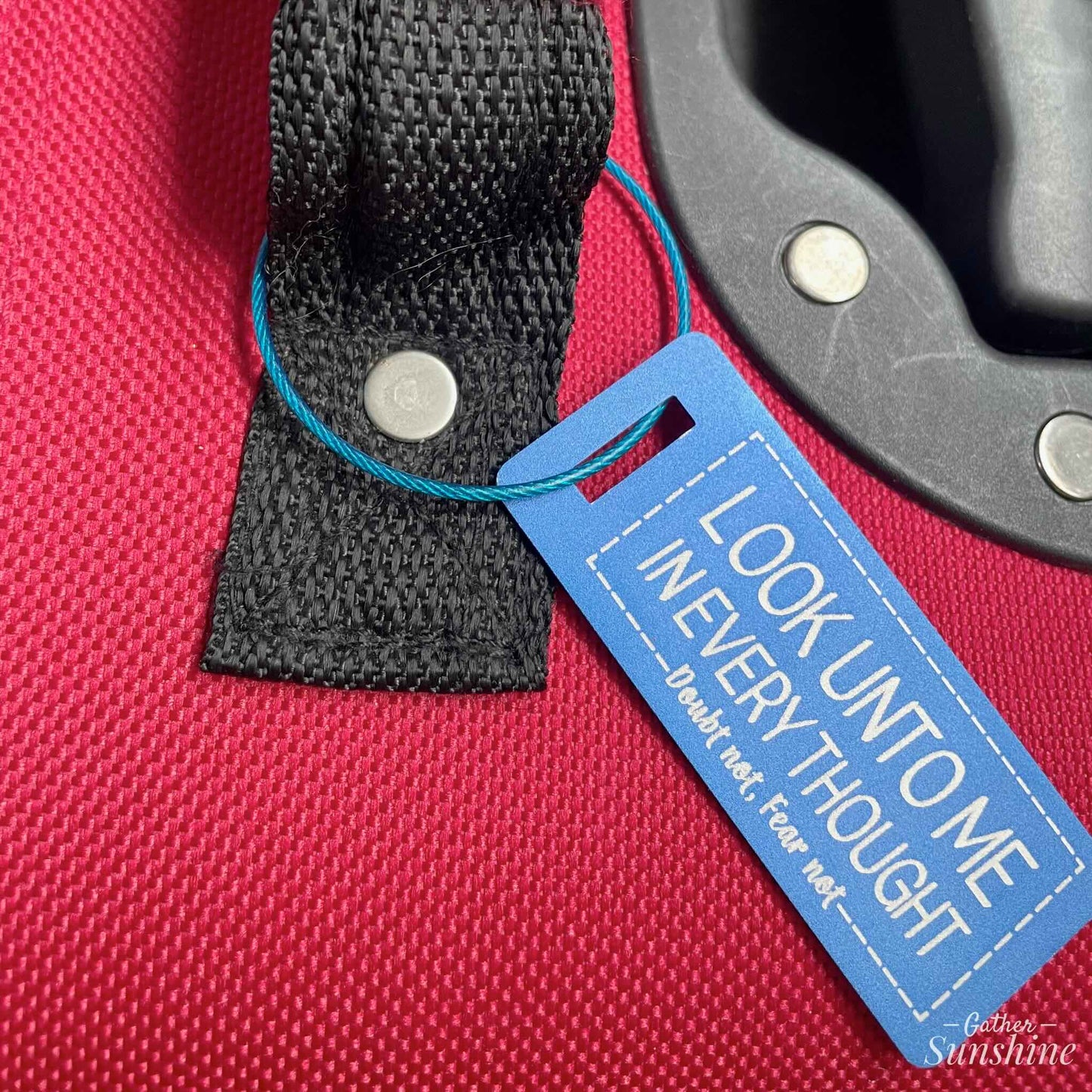 Small (3"x1") blue luggage tag with motivational text "Look Unto Me In Every Thought, Doubt Not, Fear Not" on red suitcase by Gather Sunshine.