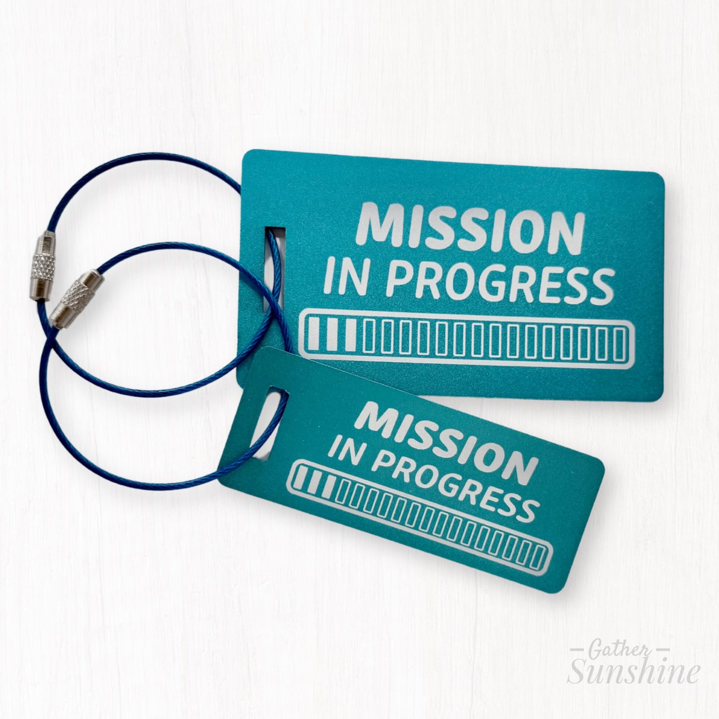 Two teal aluminum luggage tags engraved with “Mission in Progress” and 18 progress bars. LDS mission gift by GatherSunshine.