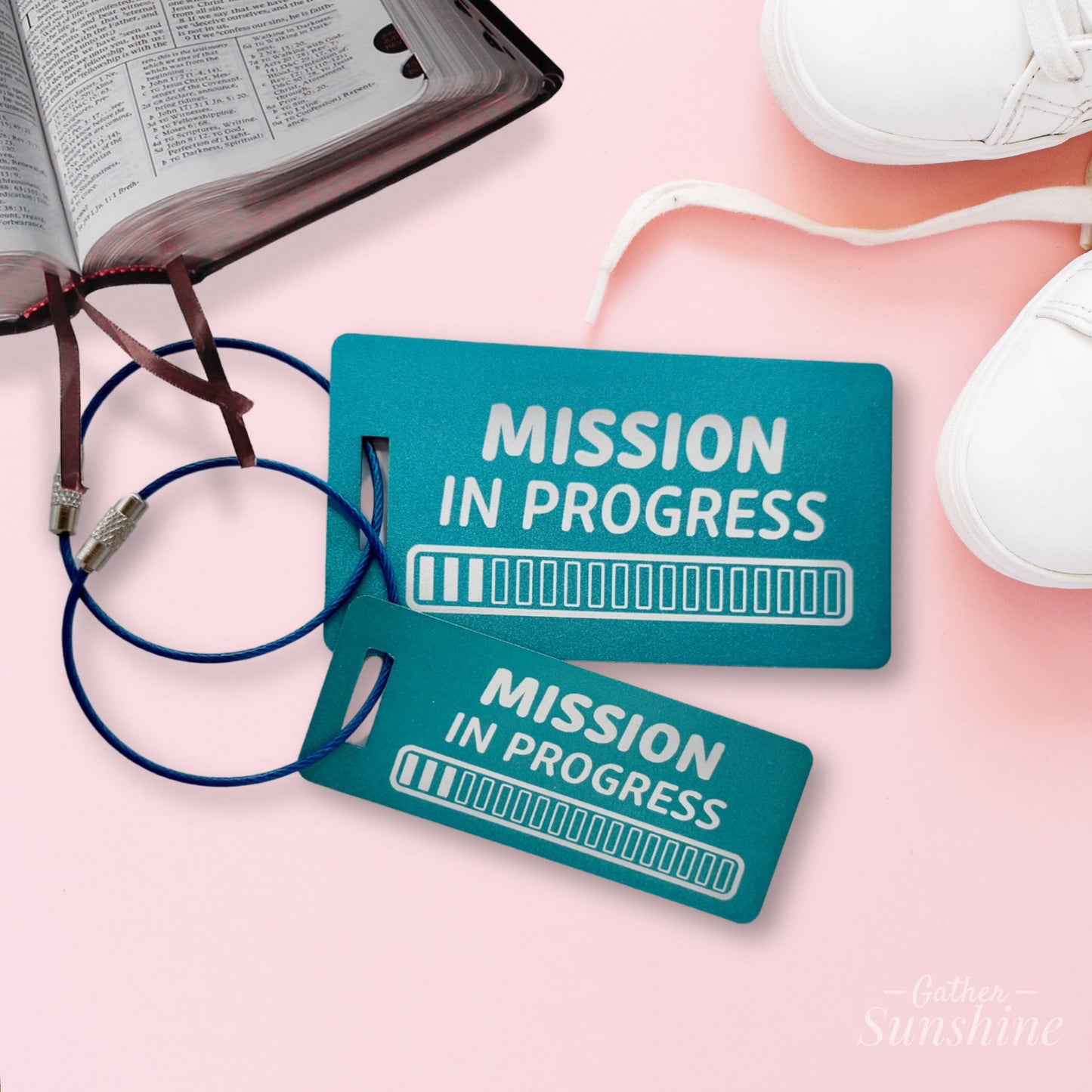 Two teal luggage tags engraved with “Mission in Progress” and 18 progress bars, displayed on a pink surface with books and shoes. LDS mission gift by GatherSunshine.
