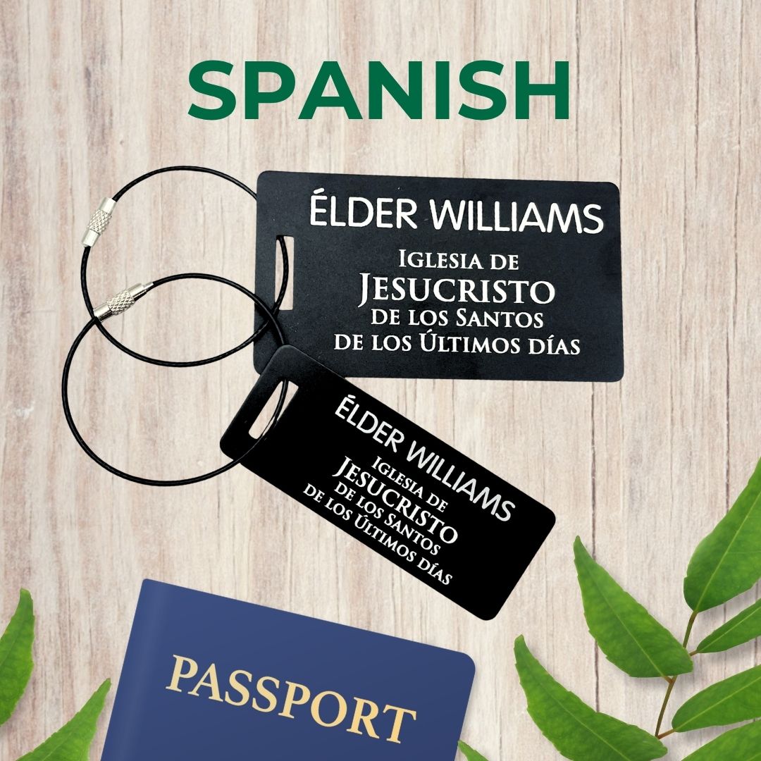 Small (3x1 inch) and large (3.5x2 inch) black luggage tags inspired by LDS missionary name tags, in Spanish with personalized name, on a wooden surface with leaves and a passport.