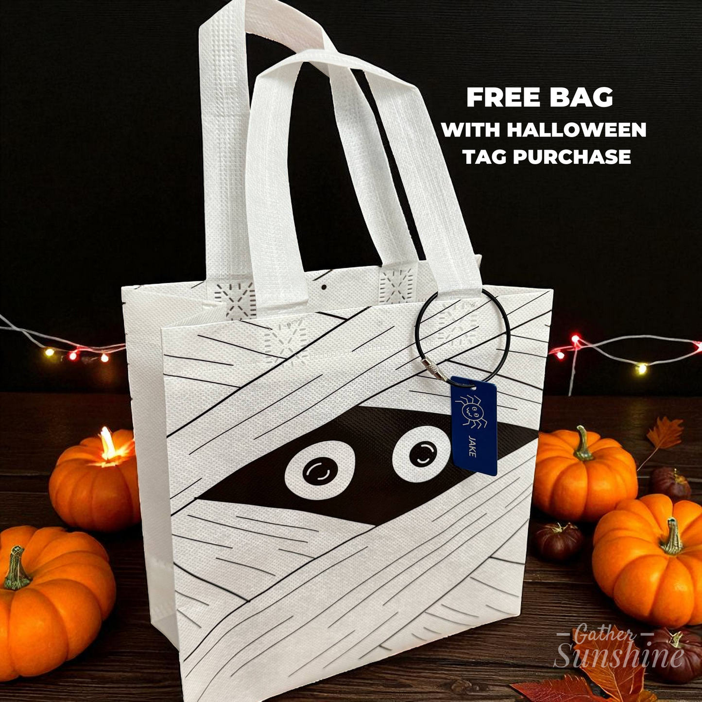 White mummy face trick-or-treat bag with engraved spider name tag personalized with child’s name, with leaves and pumpkins by Gather Sunshine.
