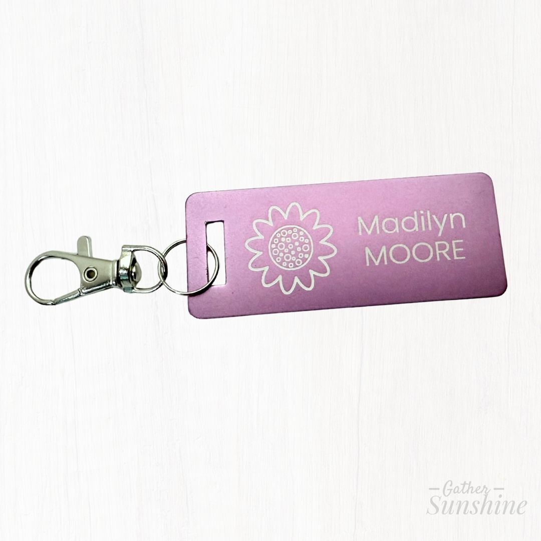 Purple backpack tag with a sunflower design and text on a white background