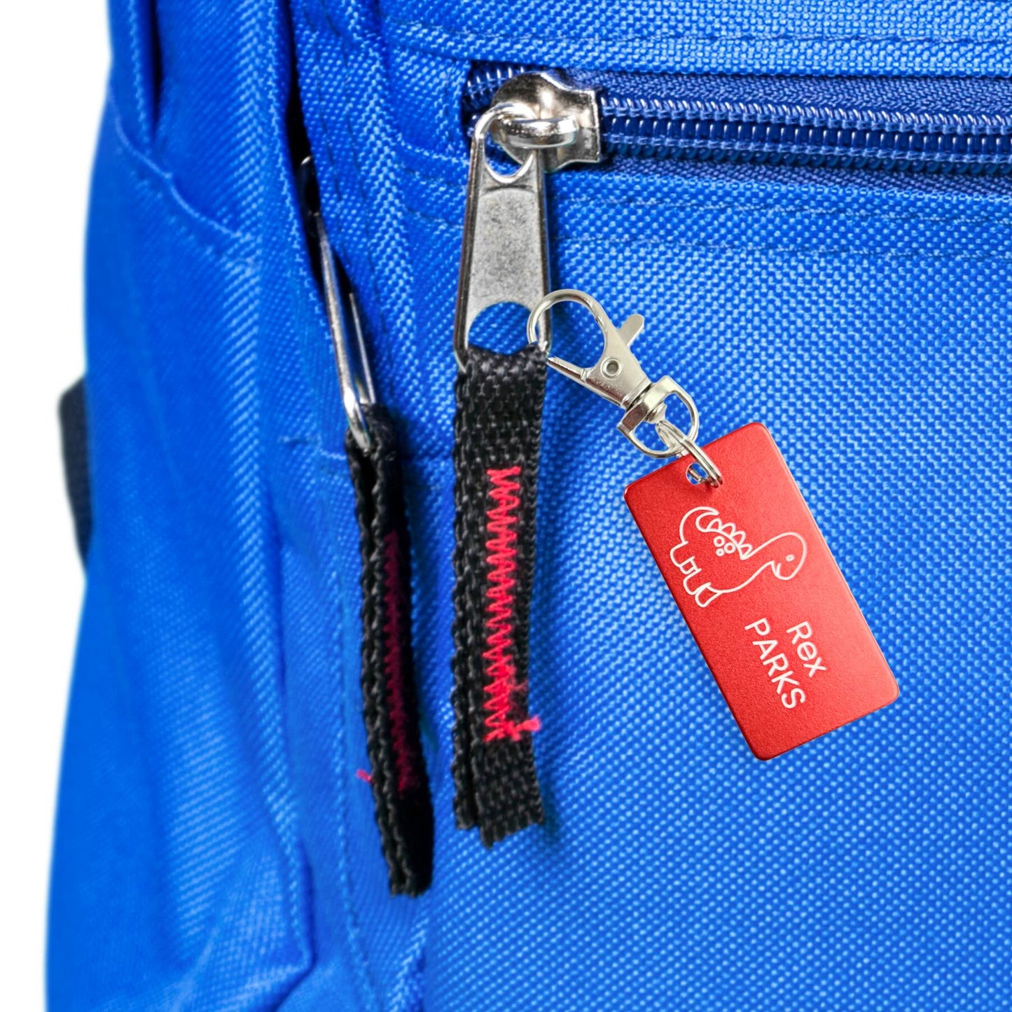 Close-up of red dinosaur kids tag on blue backpack. 1x2 inch engraved tag with clasp, perfect for school bags