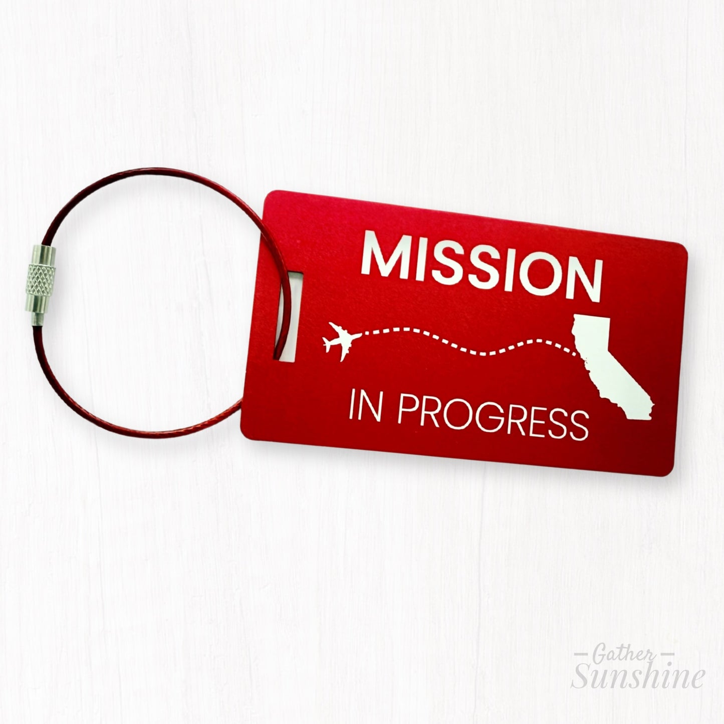 Red engraved luggage tag with “Mission in Progress” and dotted-line airplane flying toward California; ideal LDS missionary gift.