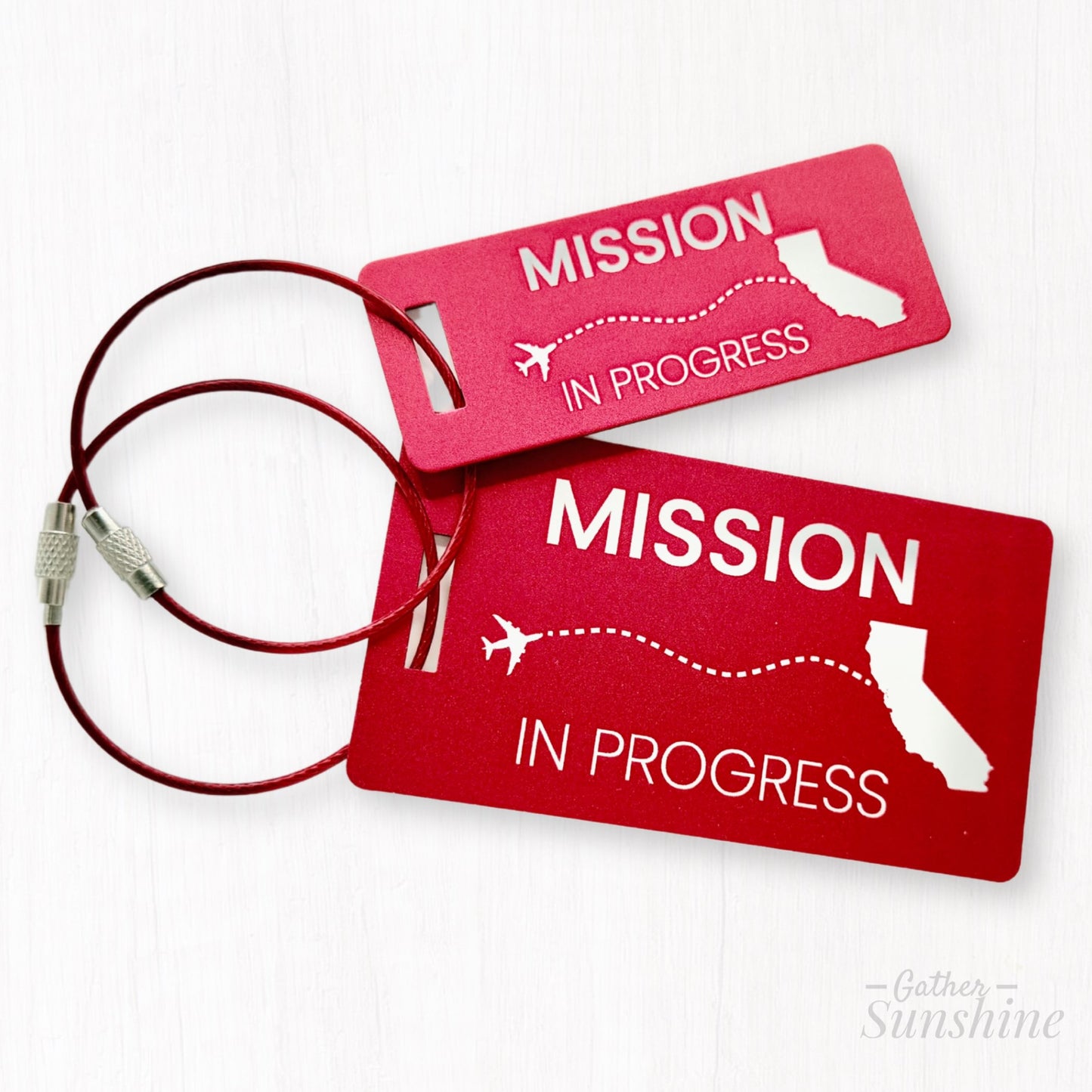 Set of red “Mission in Progress” luggage tags in small and large sizes, with dotted-line airplane flying toward California. Personalized LDS missionary gift by GatherSunshine.