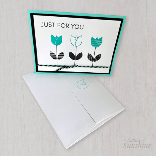 Handmade aqua and black flower card with “Just for you” stamp, layered cardstock, resting on coordinating envelope by Gather Sunshine