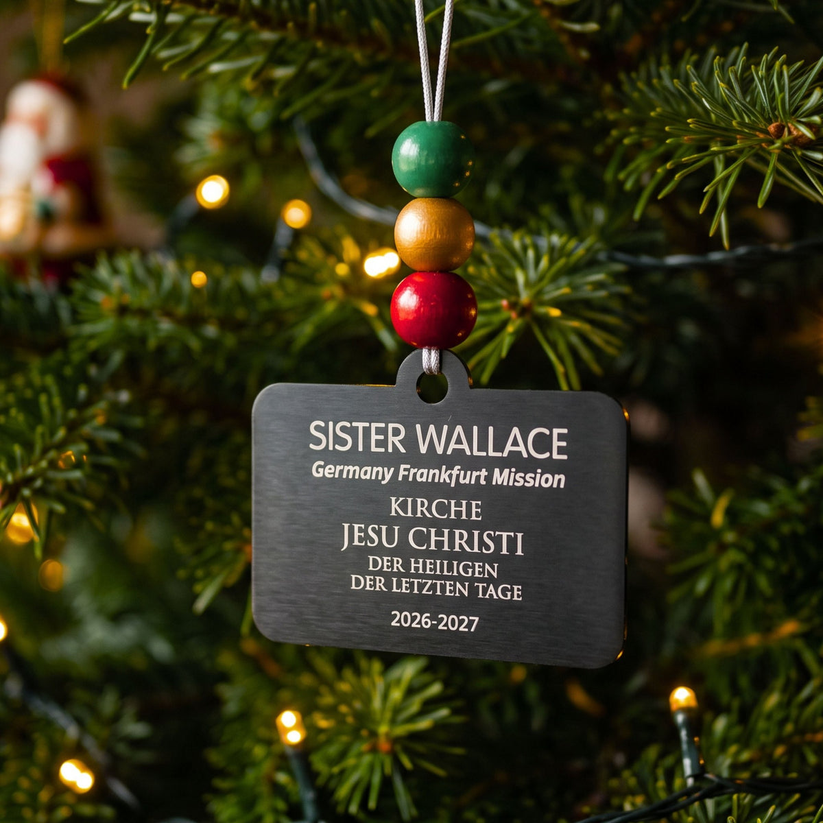 German-language Sister missionary name tag ornament with green, gold, and red beads on a Christmas tree.