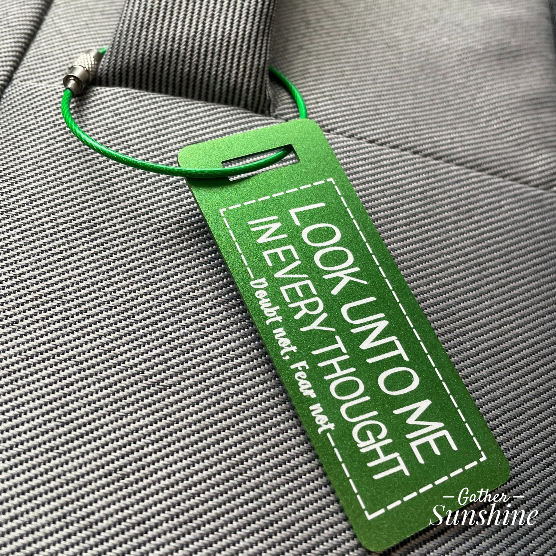 Small (3"x1") green luggage tag with motivational text "Look Unto Me In Every Thought, Doubt Not, Fear Not" attached to gray suitcase by Gather Sunshine.