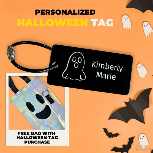 Personalized Halloween tag with engraved ghost design on black metal tag and free iridescent ghost bag, styled with bats and ghosts on orange background. By Gather Sunshine
