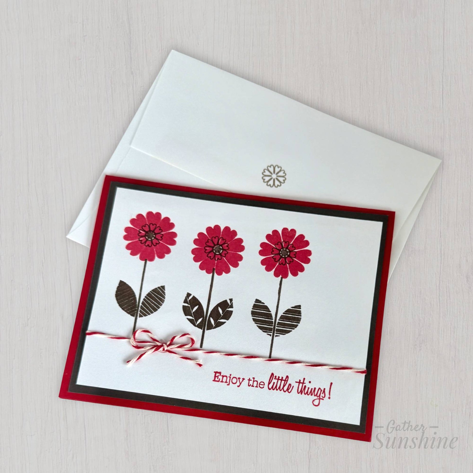 Handmade red and black flower card with stamped flowers and layered cardstock, and text "Enjoy the little things!" resting on coordinating envelope by Gather Sunshine