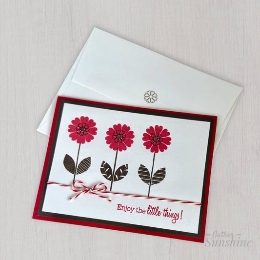 Handmade red and black flower card with stamped flowers and layered cardstock, and text "Enjoy the little things!" resting on coordinating envelope by Gather Sunshine