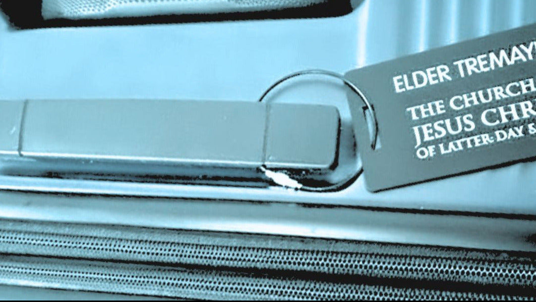 Close-up of engraved missionary luggage tag attached to suitcase zipper, durable black metal tag by Gather Sunshine